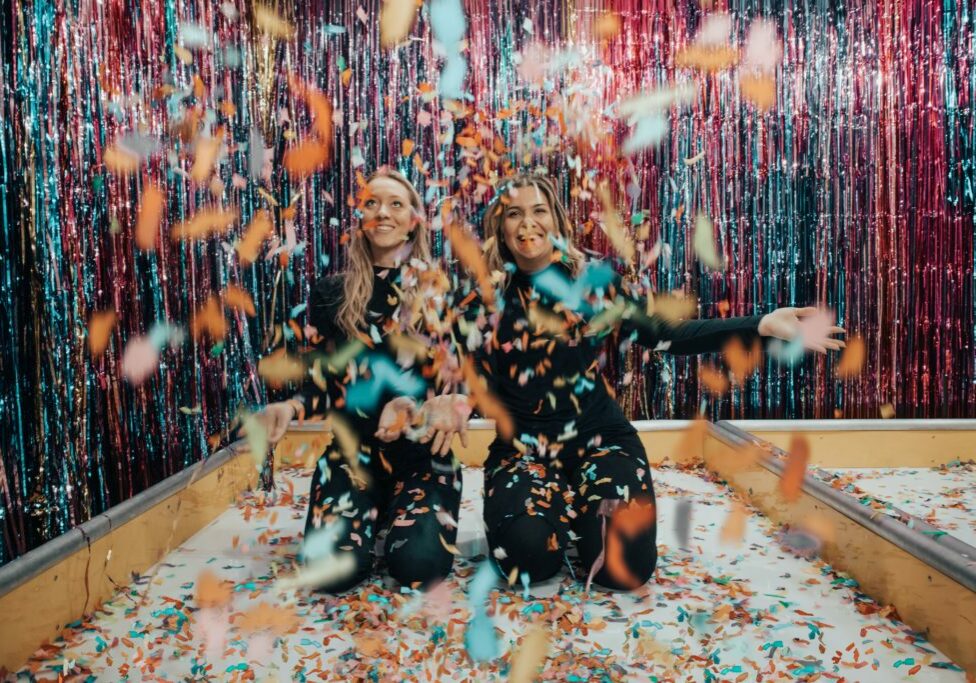 two-women-kneeling-while-throwing-confetti-1627935